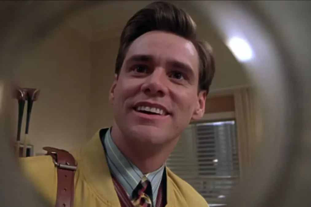 Jim Carrey as Truman Burbank smiling in a yellow jacket, seen through a peephole-style lens in The Truman Show