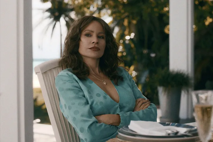 Sofía Vergara as Griselda Blanco in a teal blouse, arms crossed, sitting at an outdoor table