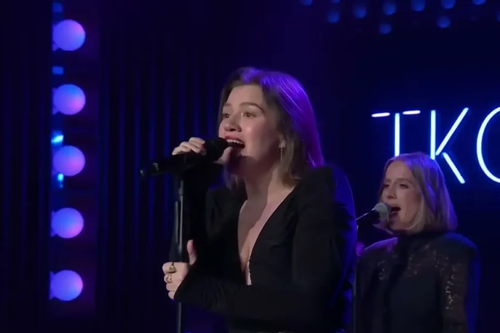 Kelly Clarkson in a black blazer singing into a microphone on the stage of The Kelly Clarkson Show