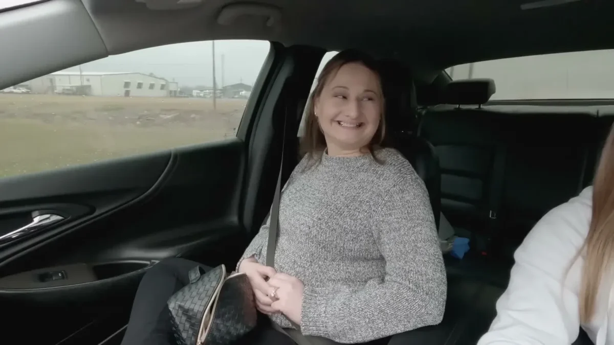 Gypsy Rose Blanchard smiling in the back seat of a car in a gray knit sweater