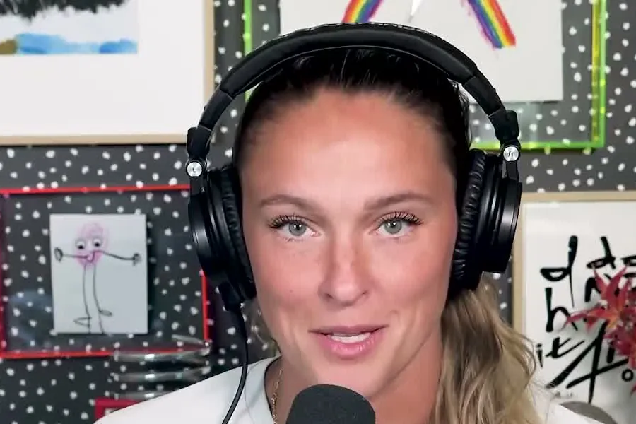 Kylie Kelce in a white top and headphones with a ponytail smiling at the Not Gonna Lie microphone