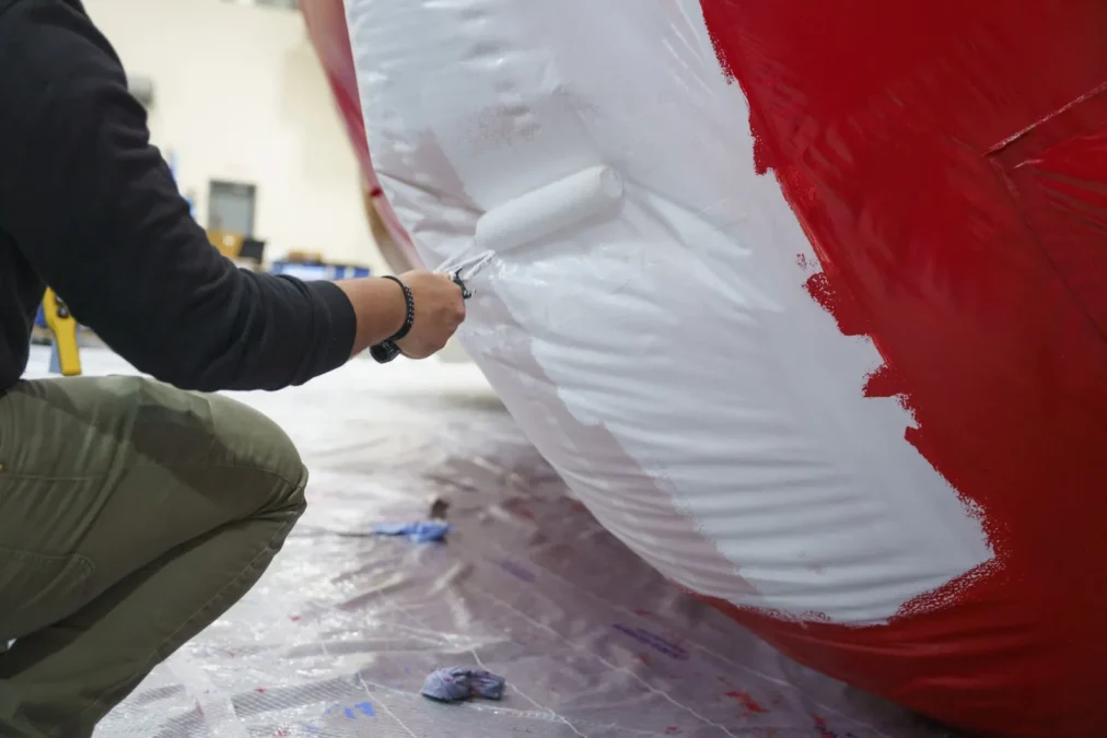 A worker painting the white glove of the Sorcerer's Apprentice Mickey parade balloon with a roller