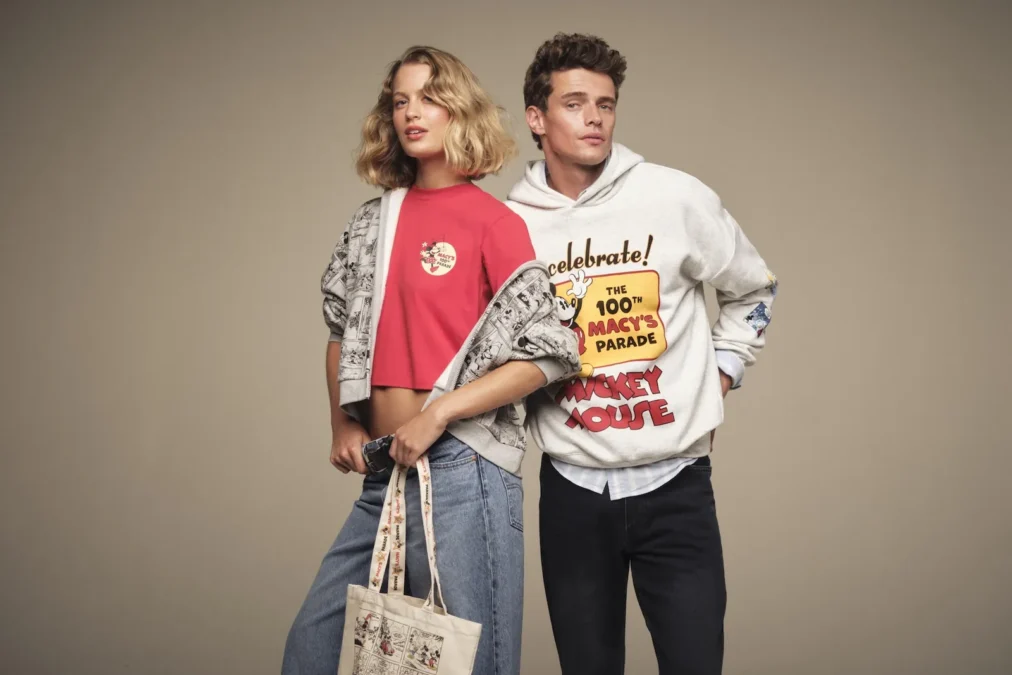 A woman in a red Minnie Mouse crop T-shirt and a comic strip jacket next to a man in a Celebrate the 100th Macy's Parade Mickey Mouse hoodie