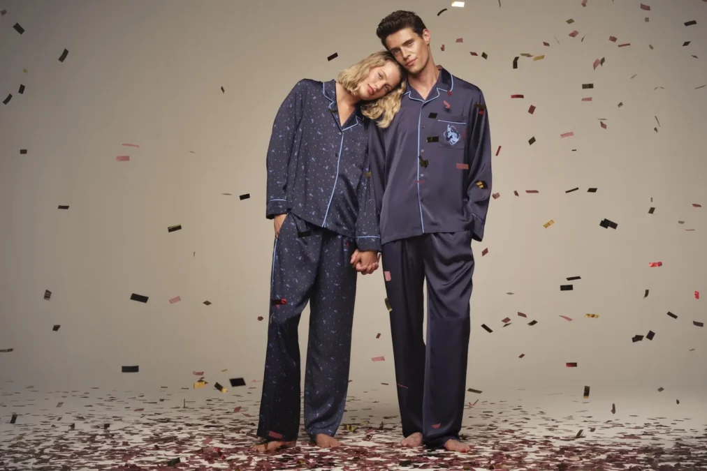 A man and a woman in navy satin pajama sets with Sorcerer's Apprentice Mickey prints, standing in falling confetti