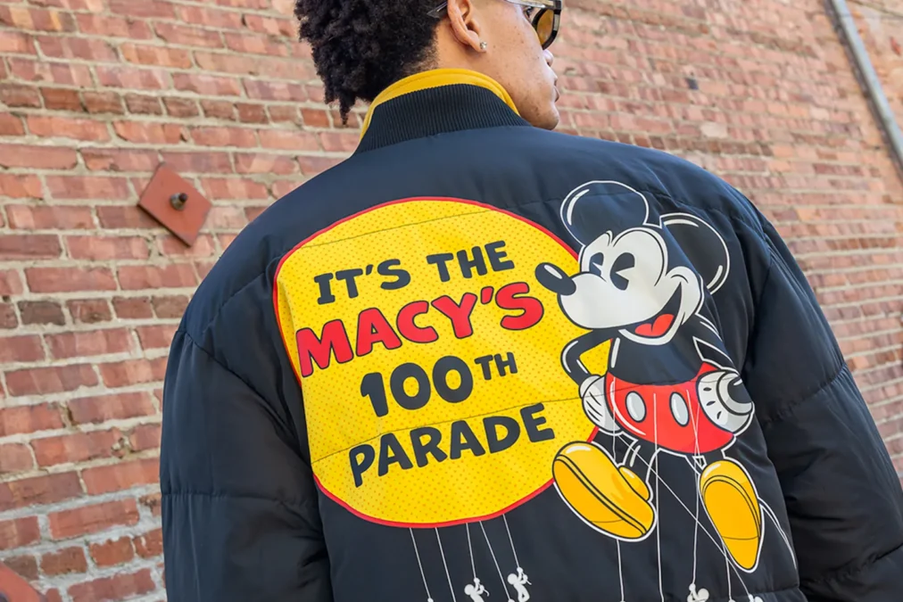The back of a navy puffer jacket with a yellow It's the Macy's 100th Parade patch and Mickey Mouse