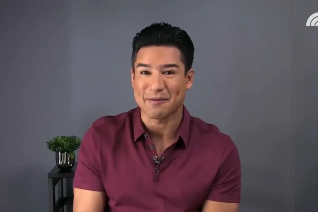 Mario Lopez in a maroon polo smiling during a video interview in front of a gray backdrop