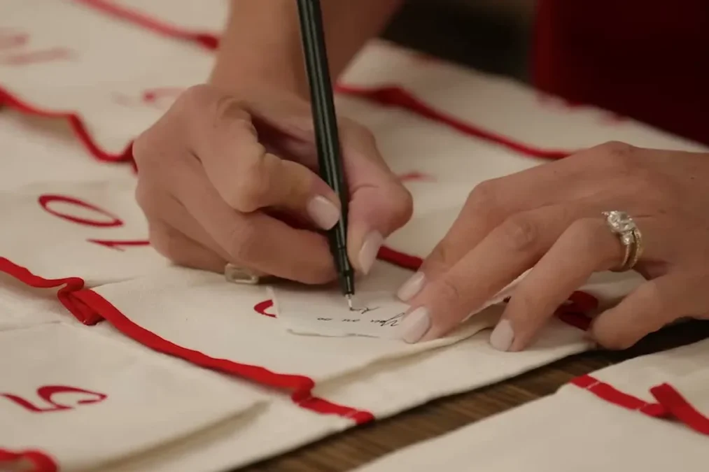 A hand writing a number in black pen on a cream fabric advent pouch trimmed in red ribbon