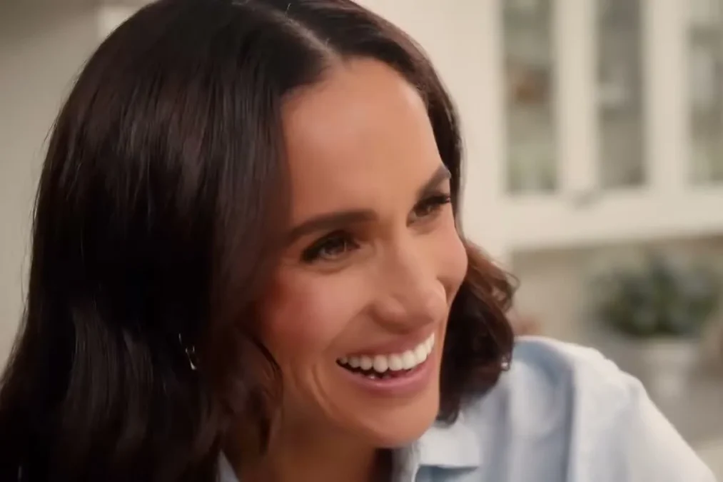 Meghan Markle smiling in a light blue shirt in a white kitchen in the trailer for With Love, Meghan