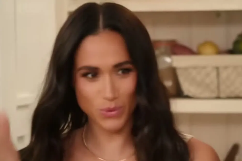 Meghan Markle with long dark hair in a white top looking to the side in a kitchen in the trailer for With Love, Meghan