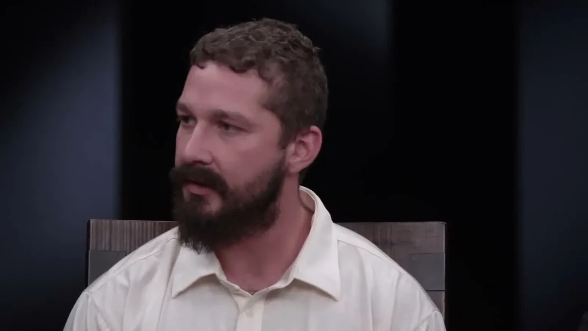 Shia LaBeouf with a full beard and a cream shirt, seated during a filmed interview