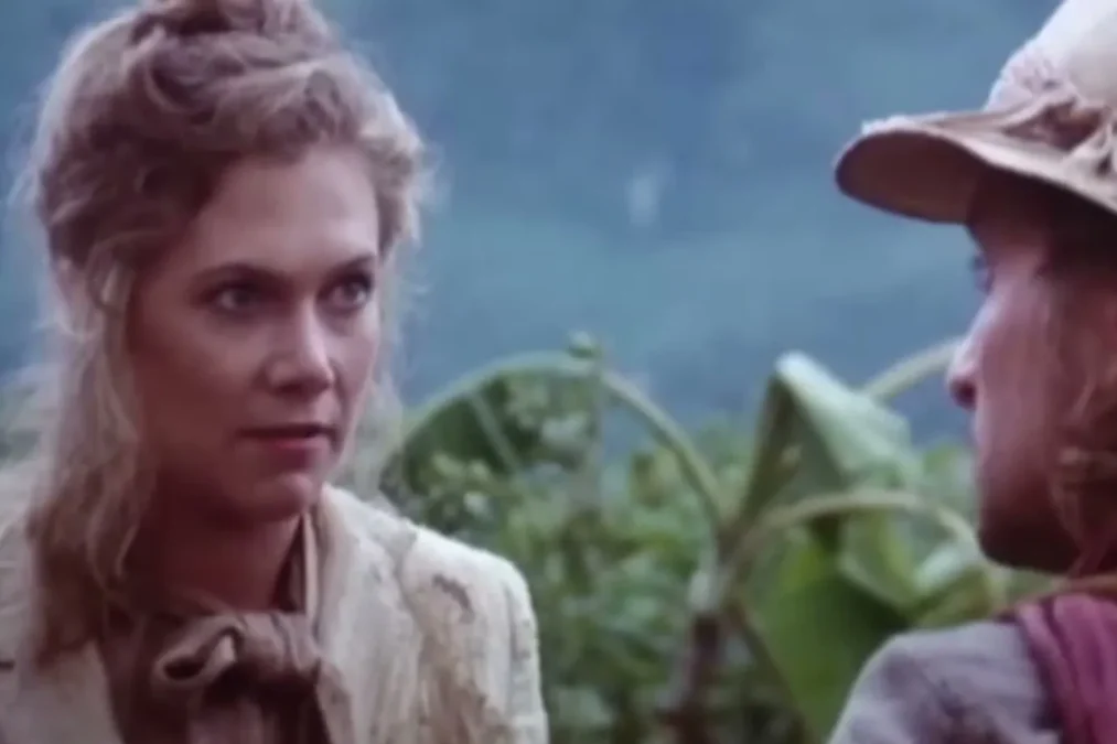 Kathleen Turner in a rumpled cream jacket looking at Michael Douglas, in profile in a safari hat, in a jungle scene from Romancing the Stone