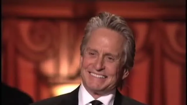 Michael Douglas in a black suit and tie smiling at a tribute dinner