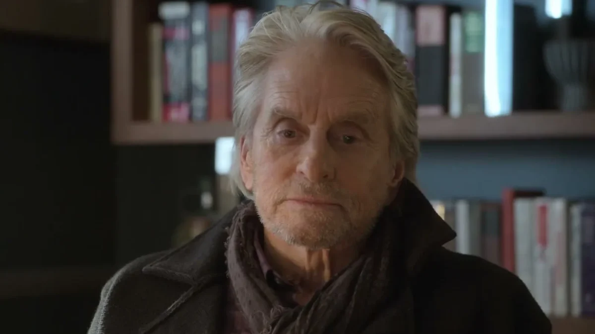 Michael Douglas in a dark jacket and scarf in front of a bookshelf in The Kominsky Method