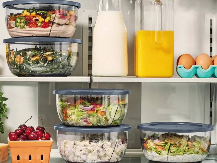 Five Ninja PREPi bowls with gray storage lids stacked on refrigerator shelves, filled with salads and chicken salad