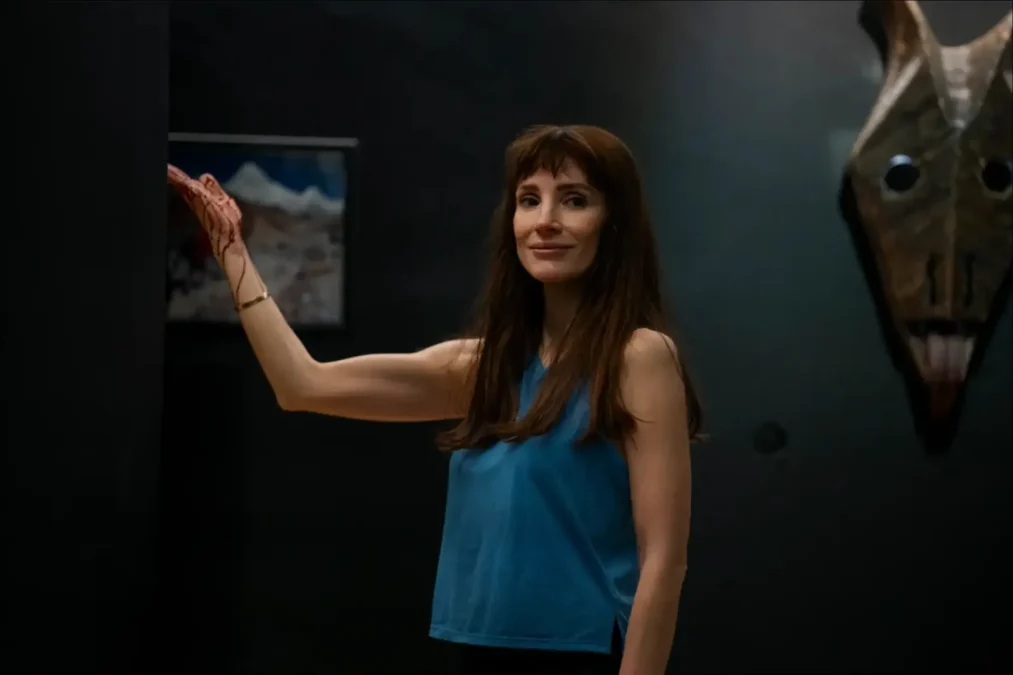Jessica Chastain in a blue tank top reaching toward a dark wall in a dim room