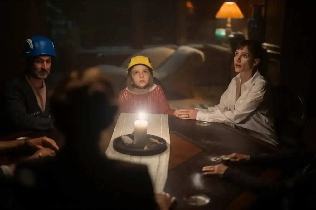 Several people holding hands around a candlelit table, a man and a girl wearing hard hats