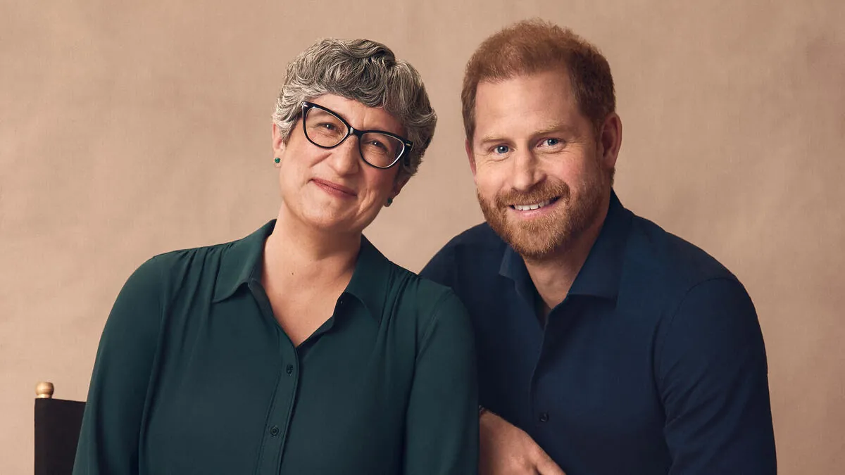 Prince Harry in a navy shirt smiling next to Dr. Mary-Frances O'Connor, who wears glasses and a green blouse, in a studio portrait