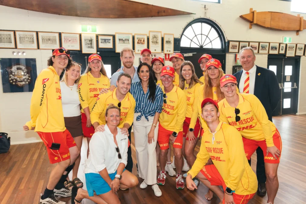 Prince Harry and Meghan posing with lifesavers in red and yellow uniforms inside a clubhouse