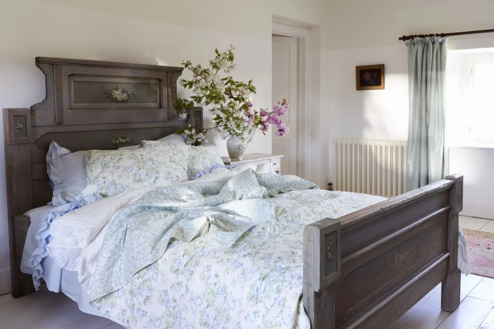A dark wood bed with a light blue floral quilt, light blue ruffled sheets and floral pillows
