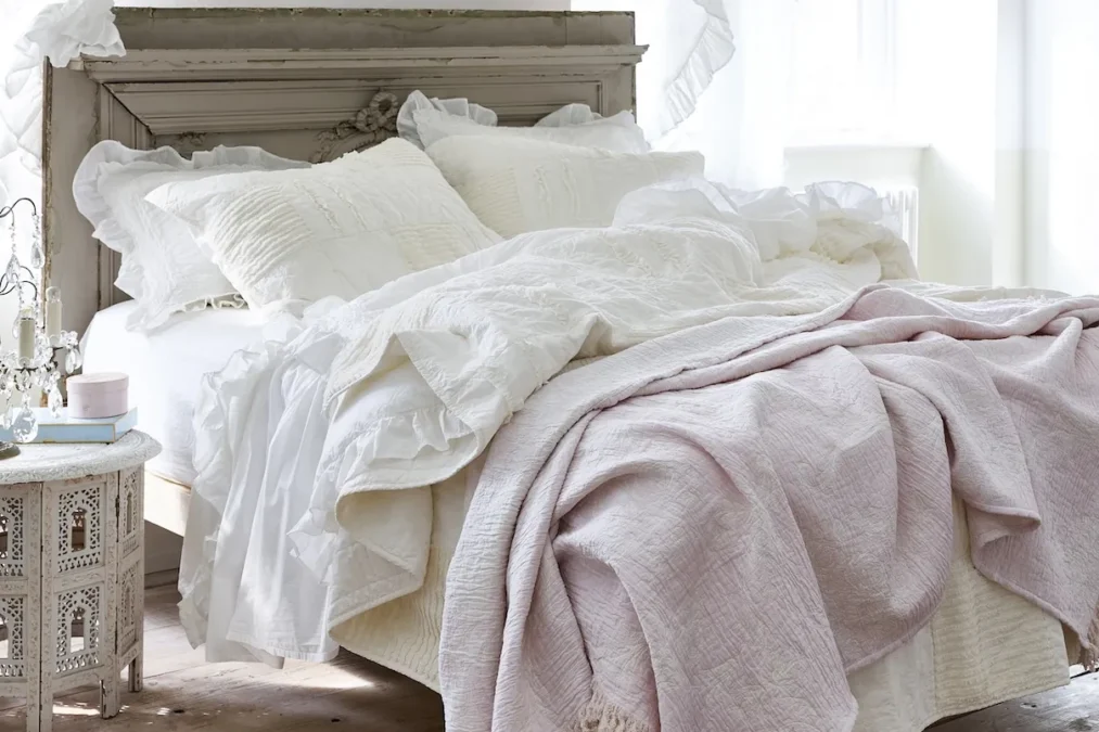 A white patchwork quilt topped with a pink blanket on a bed with white pillows