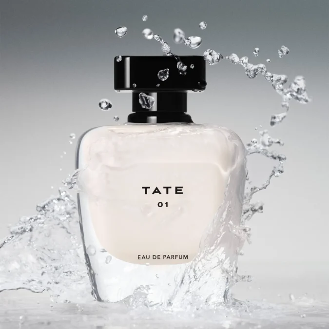 The TATE 01 eau de parfum bottle, a rounded glass bottle with a black cap, surrounded by a splash of water