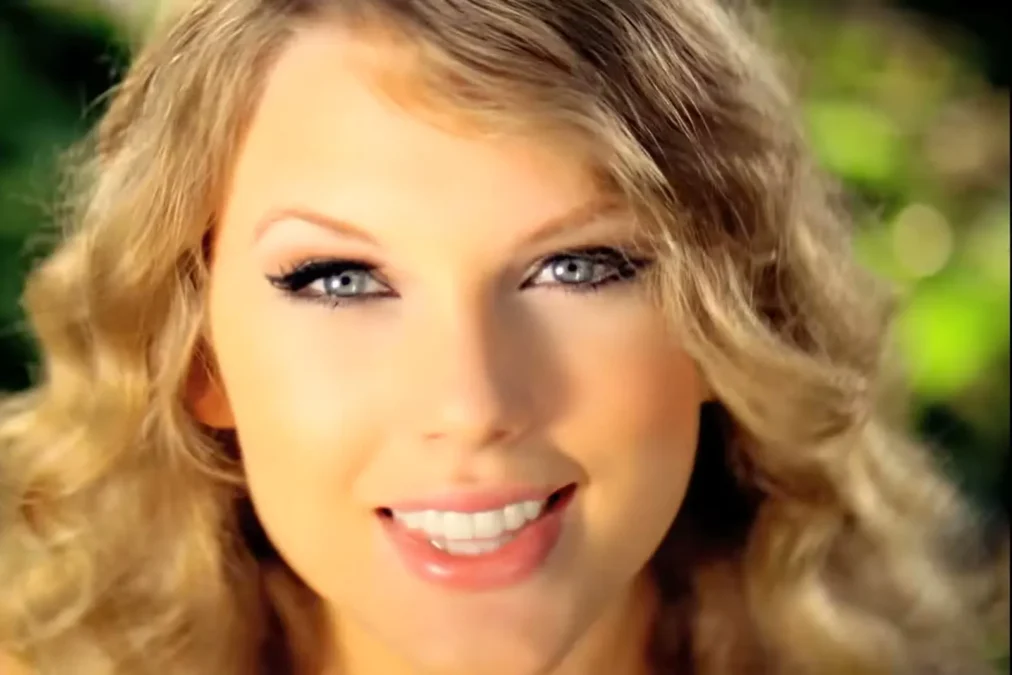 Close-up of a young Taylor Swift smiling, with long blond ringlets, in the music video for Mine