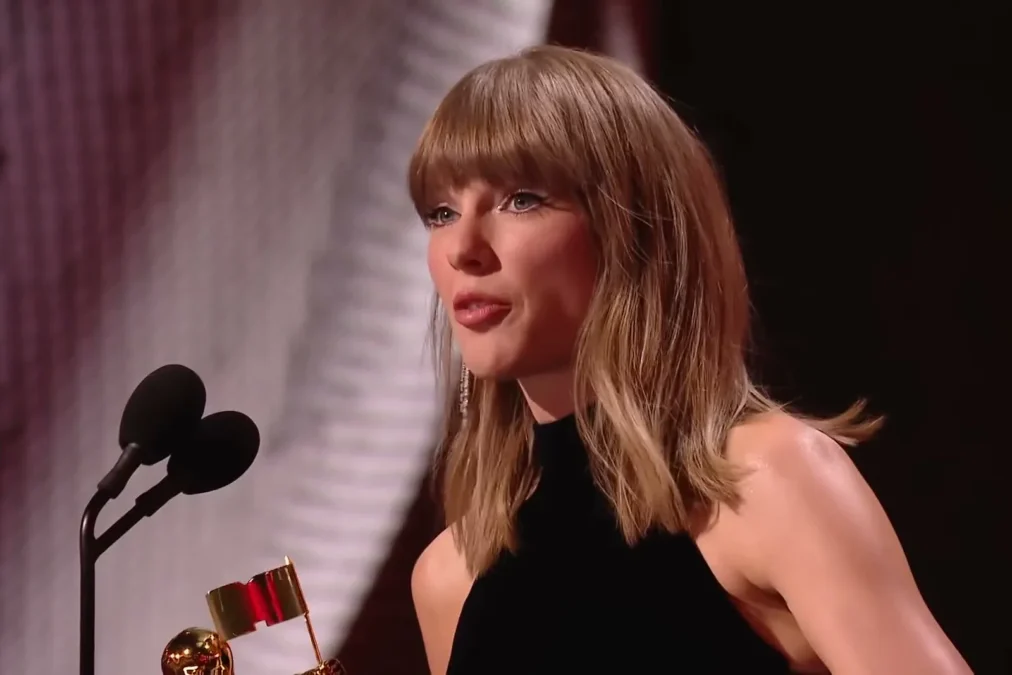 Taylor Swift with a straight, shoulder-length lob and bangs, in a black halter top, speaking at a microphone at the 2026 MTV VMAs