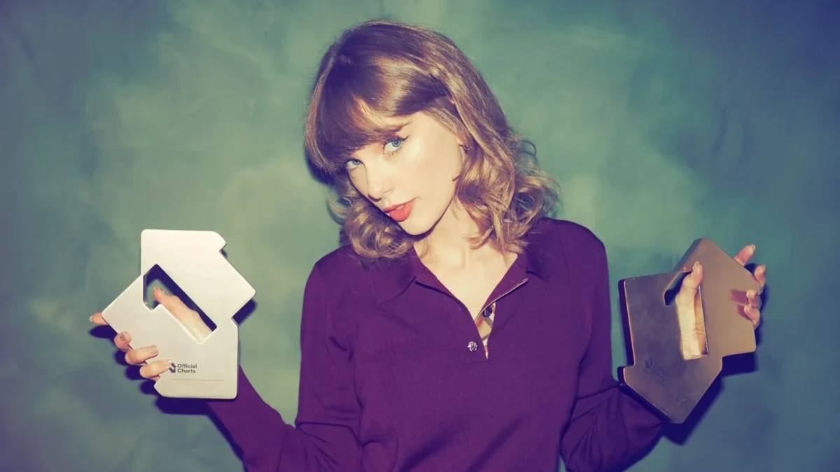 Taylor Swift with a curly, collarbone-length lob and full bangs, in a burgundy sweater, holding two Official Charts trophies