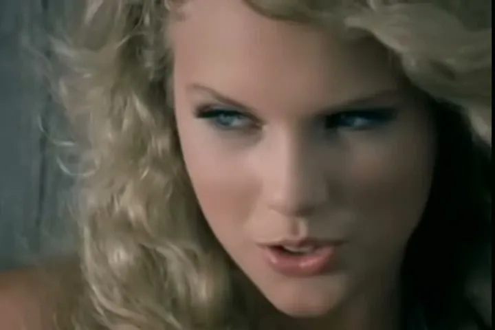 Teenage Taylor Swift with curly blond hair looking sideways in the music video for Tim McGraw
