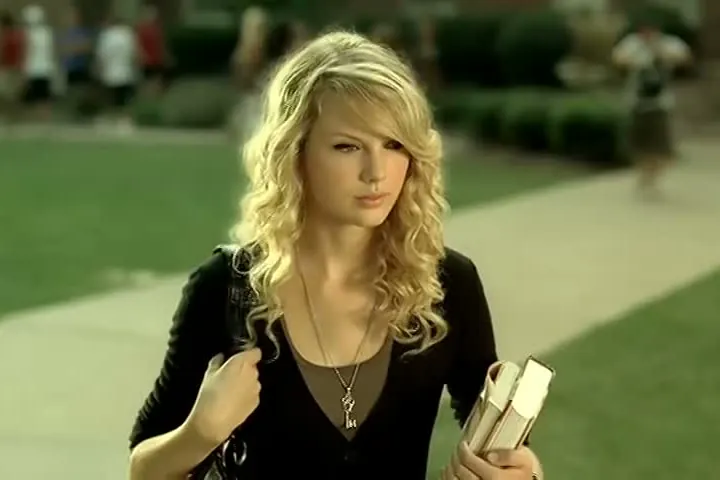 Taylor Swift with long curly blond hair, carrying books on a college campus in the Love Story music video