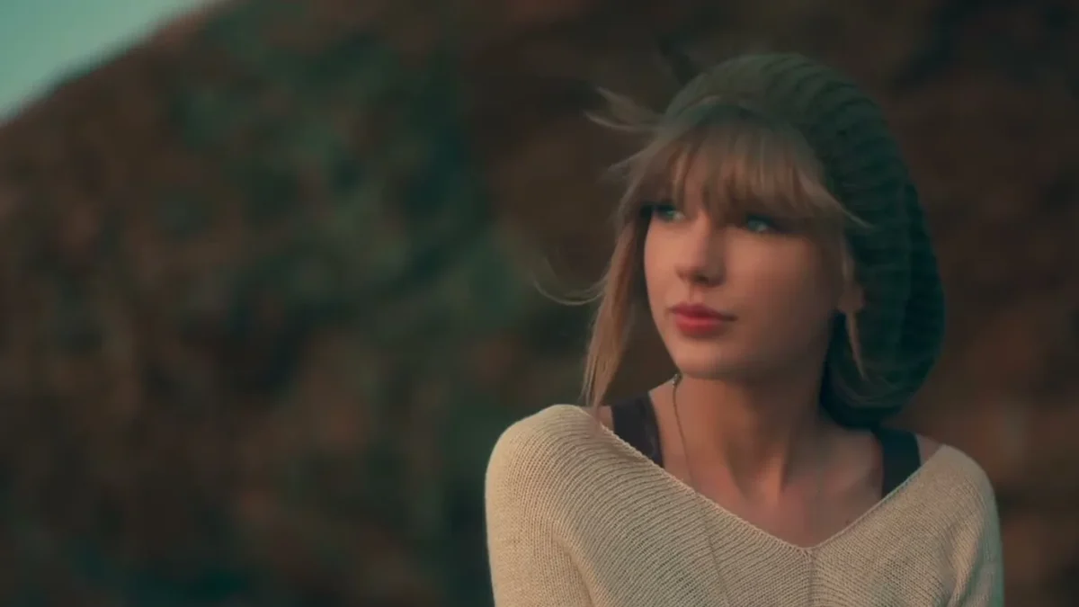 Taylor Swift with straight hair and blunt bangs under a green knit beanie in the 22 music video