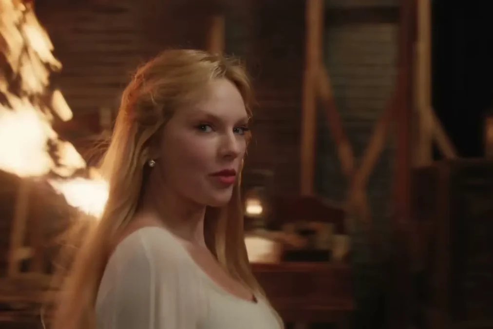 Taylor Swift with long strawberry-blond hair in a white dress in a theater set in The Fate of Ophelia music video