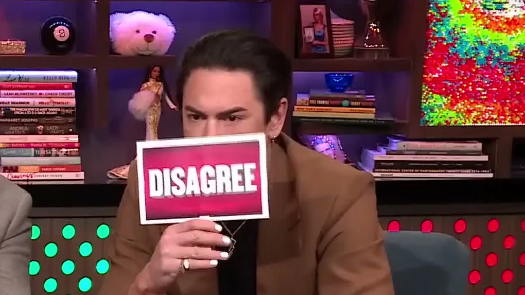 Tom Sandoval in a brown suit holding a Disagree sign on Watch What Happens Live